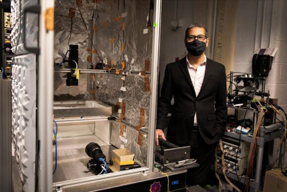 Venki Murthy, in a mask, standing amid a suite of technology