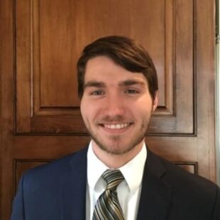 Daniel Ritter wearing a suit and tie and smiling at the camera.