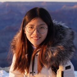 Ruojin Cai wearing a white jacket with a brown fur-lined hood, smiling at the camera.